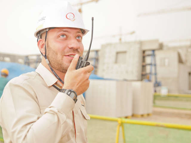 Man in hard hat using handheld radio at industrial site